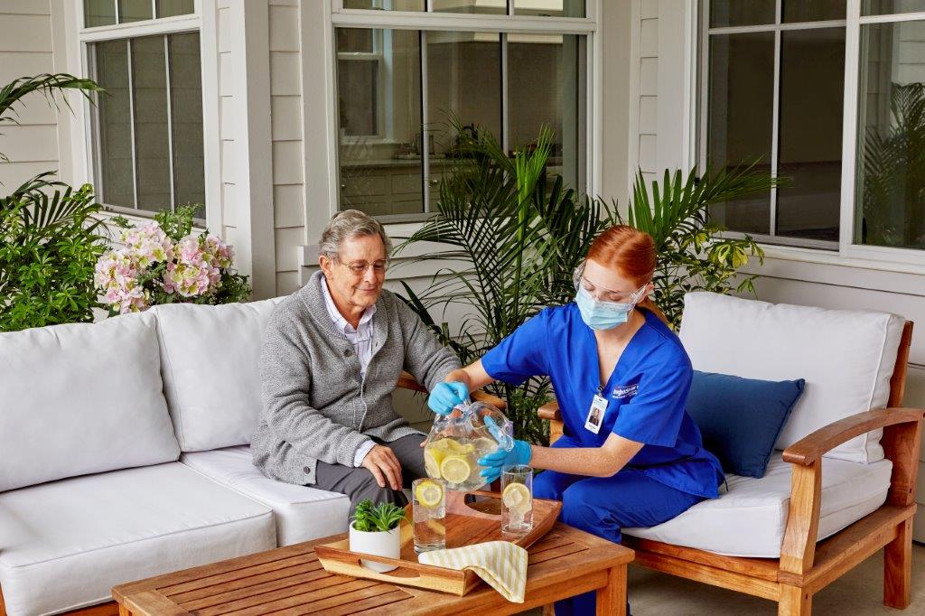 An older man sits with his BrightStar Care healthcare provider outside while she pours lemonade.